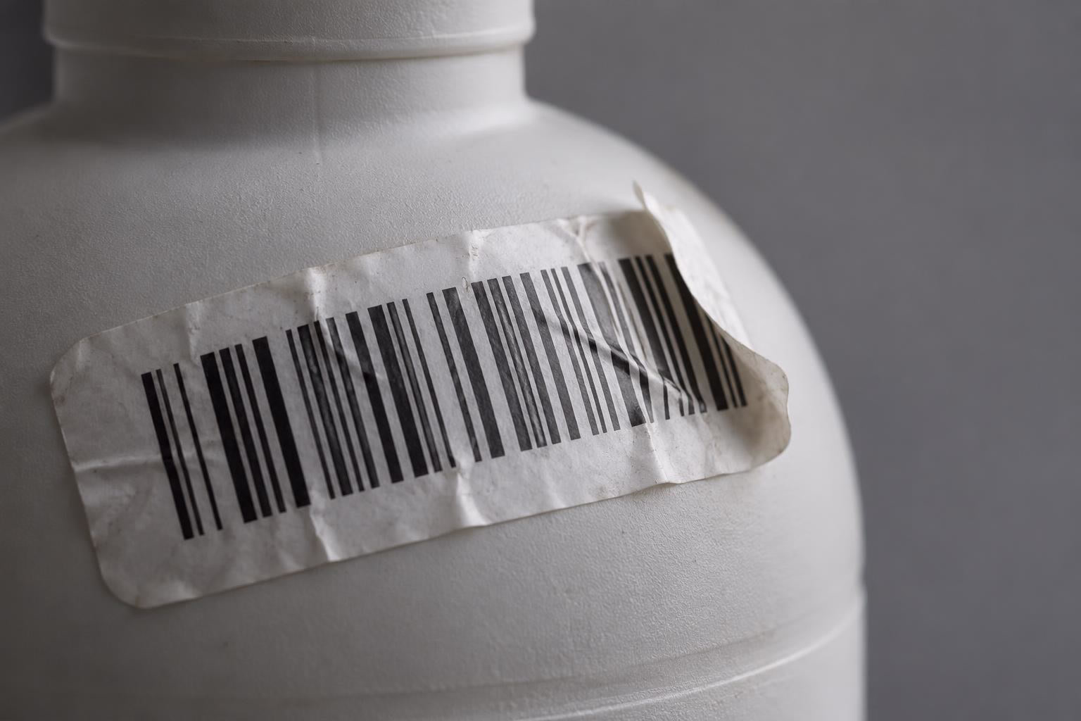 Une étiquette code-barres froissée se décolle de l'épaule bombée d'un flacon plastique